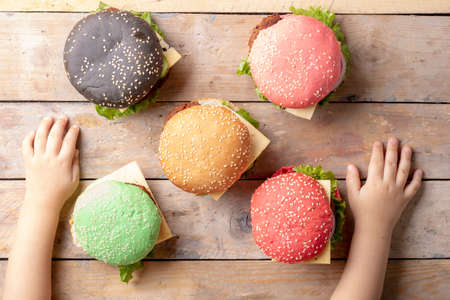 Kids hands and colorful bugerss with selective focus on the foreground burger, top view