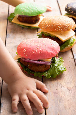 Kids hands holding colorful burgers with vegetables. Fast food or street food unhealthy.の写真素材