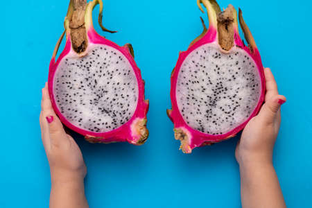 Close up cropped photo of female hold in hand fresh half pitahaya, dragon fruit blue paper, top viewの写真素材