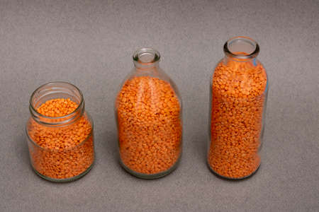 Three jars with orange and red lentil on table, legumes concept, horizontal food photoの写真素材