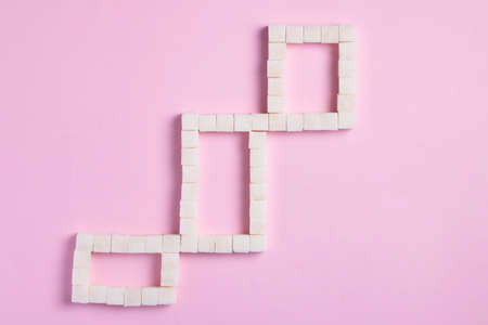 Sugar cubes are laid out in the form of a small squares on pink background, creative design food...