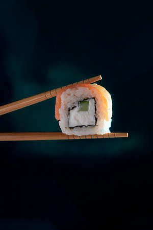 hand holding chopstick with to eat Philadelphia Sushi roll on blak backgroundの写真素材