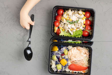 girl holds spoon to eat school lunch into food containers, raw vegetables for health, flat lay and place for textの写真素材