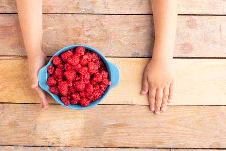 Kids hands holding blue bowl with strawberries on wooden background, flat layの写真素材