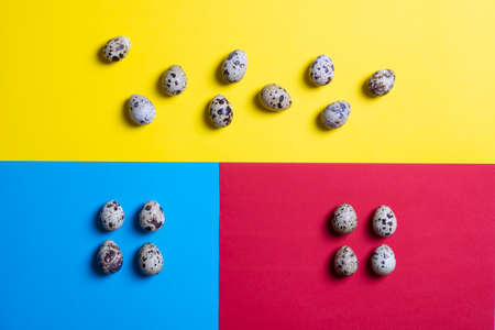 Decor colorful Easter quail eggs on pink, blue and yellow papers. Top view with copy space....