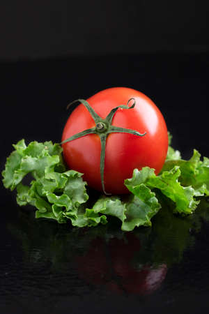 Red tomato on leaf lettuce. Vertical photo, dark key and copy spaceの写真素材