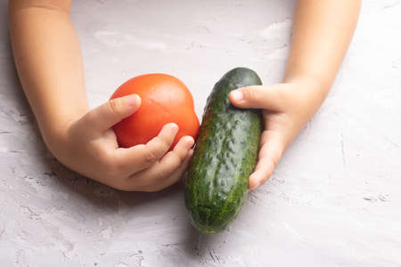 Kids hands holding raw fresh seasonal vegetable. Cucumber, tomatoe, top viewの写真素材