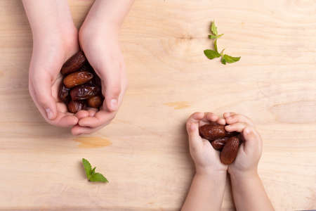 Ramadan concept. Kids holding dried date on old wooden table, Flat lay and top view