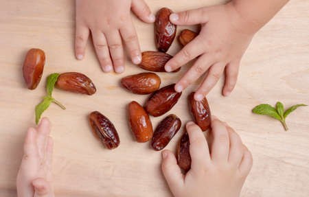 muslim lifestyle meal. Ramadan dates , mint and kids hands holding dates onwooden table. Top viewの写真素材