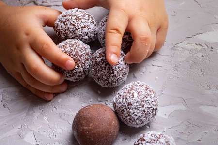 Baby holding healthy energy balls, chocolate balls for breakfast. No gluten concept food