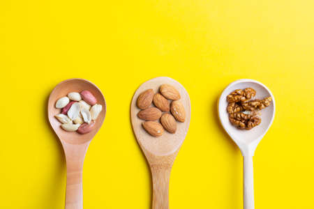 Peeled nuts in spoons, raw dried nuts on yellow