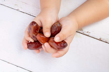Many Dried date fruits in kids palms. Hands holding dates