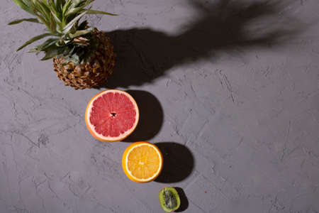 Exotic fruits ananas, ananas, pineapple, orange and kiwi on gray table, flat lay