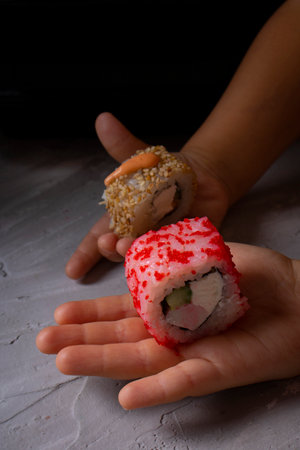 sushi rolls in kids hands on a dark background, vertical imageの写真素材