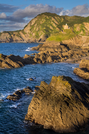 Colorful seascape with rocky coastline. The low evening sun. A small church on the hill. In the foreground is part of the rock. North Devon. UKの写真素材