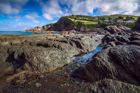 View Combe Martin from the bay at low tide. Little house on the hill.The stones in the foreground. North Devon. Englandの写真素材