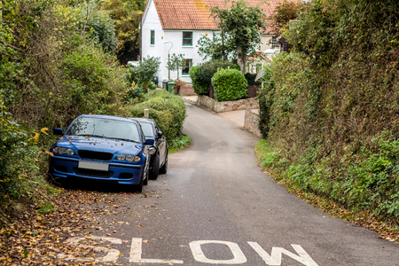 A narrow street in Exeter. White house and two cars on the roadside. On the asphalt the inscription is Slow. Devon. Englandの写真素材