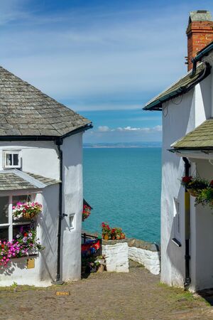 A narrow picturesque street in the small and beautiful village of Clovelly. Between the white houses you can see the sea and the distant shore of Wales. A popular tourist destination in the UK. Devon. Englandの写真素材