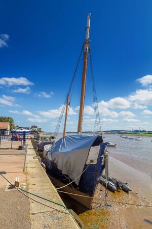 An old ship with a mast. Covered with tarpaulin. Moored at the shore at low tide. Topsham. Devon. Englandの写真素材