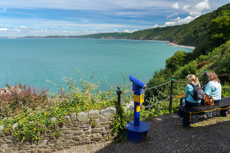 Clovelly, Devon, England, July 14, 2016: Two women sit on a bench and enjoy a beautiful view. View point.のeditorial素材