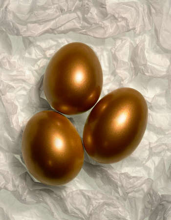 THREE GOLDEN EGGS ON WHITE TISSUE PAPERの写真素材