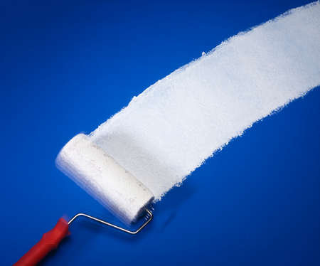 PAINT ROLLER APPLYING WHITE PAINT OVER BLUE BACKGROUND