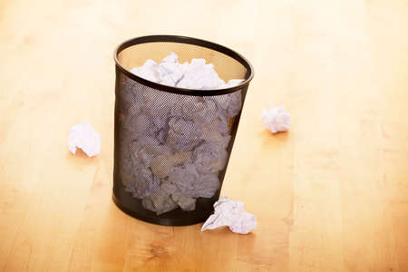 Waster paper bin full of crumpled paper on wooden floorの写真素材