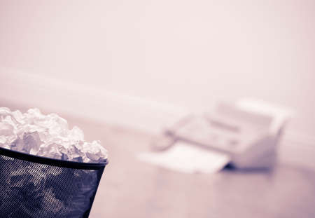Waste bin full of crumpled paper with fax machine in backgroundの写真素材