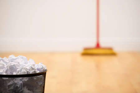 Waste bin full of crumpled paper with sweeping brush in backgroundの写真素材