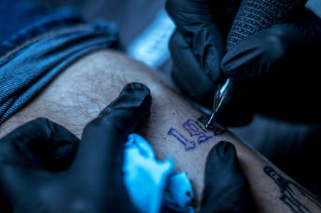 female artist tattooing letters on a client's leg