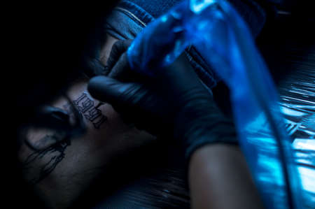 female artist tattooing letters on a client's leg