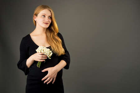 beautiful young pregnant blonde woman with flowers isolatedの写真素材