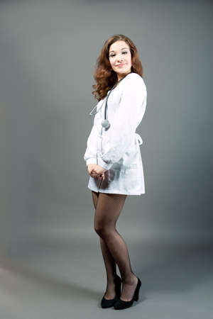 young sensual female doctor standing with smile in whites isolated over grayの写真素材