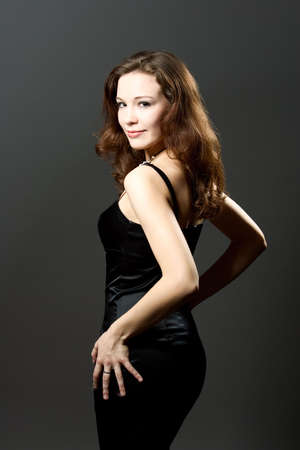 caucasian dark hair girl turned backwards in black dress isolated over gray backgroundの写真素材