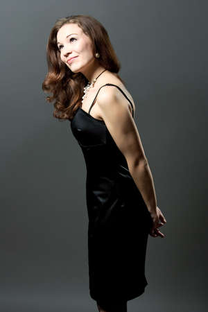 expressive funny smiling young girl in black evening dress isolated over grayの写真素材
