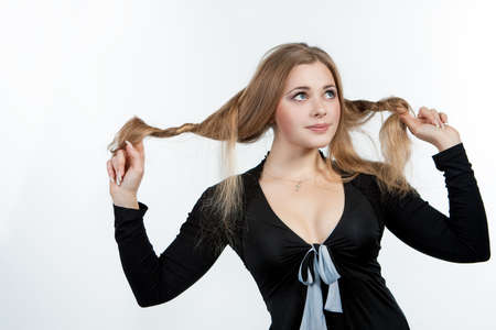 smiling and sensual caucasian blond girl standing wigh hands lifted touching hair and making cue isolated on white backgroundの写真素材