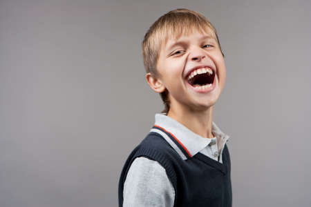 happy and sincerely laughing young caucasian teenager boy standing in sweater shot in studio isolatedの写真素材