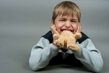 young cute teenagre with teddy bear in mouth laughing and laying on floor isolated over grayの写真素材
