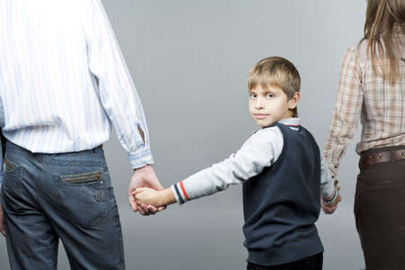 young caucasian family together with young teenager boy in middle turned backwards with smile and isolted over gray backgroundの写真素材
