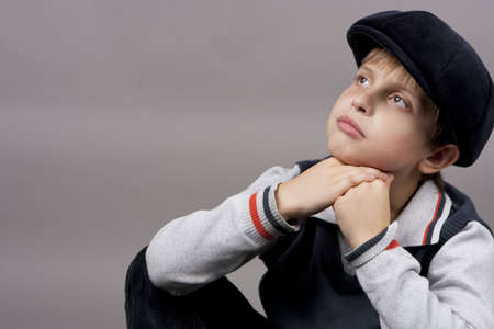 relaxing and calm teenager boy in old cap sitting with hands crossed in front and looking up isolated over gray backgroundの写真素材