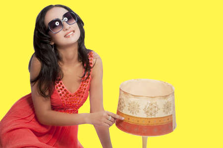 smiling and happy caucasian brunette girl sitting in sunglasses near the old lamp and having fun with playing it isolated over yellow solid backgroundの写真素材