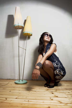 young and pretty caucasian girl in elegant sunglasses sitting in front of gray wall making a happy facial expressionの写真素材