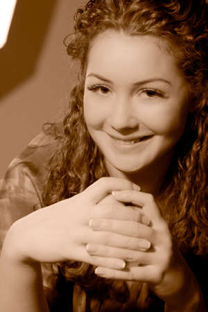 young pretty smiling caucasian girl with natural beautiful curly hair sitting in front of wall and laughing made in sepia tonalityの写真素材