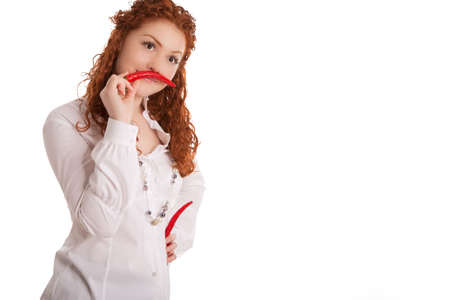 funny and beautiful young caucasian girl with red haired demonstrating whiskers made of red chilly pepper and standing isolated on white backgroundの写真素材