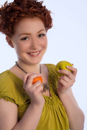 caucasian girl with positive natural smile making choice between two types of fruits isolatedの写真素材