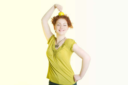 caucasian girl making an exercise with green nice apple and holding it on head with great pleasure smiling  nicely and isolated over white backgroundの写真素材