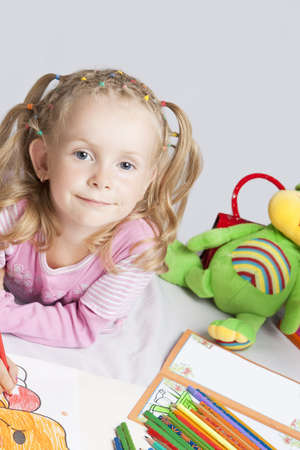smiling and happy young caucasian small girl with plenty of colorful pencils lying on florr and drawing with positive facial expressionの写真素材