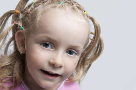 smiling caucasian blond little girl with long hair tails and playful facial expression looking from side isolatedの写真素材