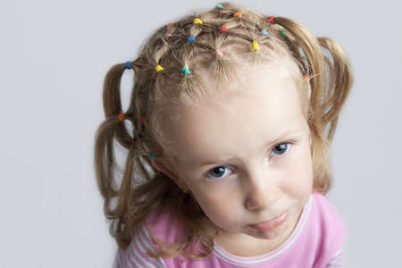 little cute caucasian blond girl making grimace with playful  facial expression having long hair tails and looking up with big blue eyes isolated over grayの写真素材