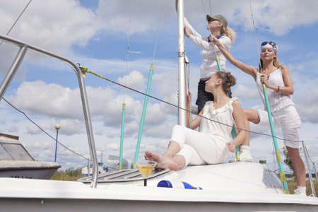 three young females with serious facial expressions standing on yacht board and expecting to set sail. shot made with studio strobe on location.の写真素材